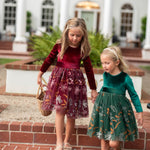 Two girls wearing burgundy and hunter green velvet floral dresses together joyful
