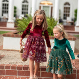 Two girls wearing burgundy and hunter green velvet floral dresses together joyful
