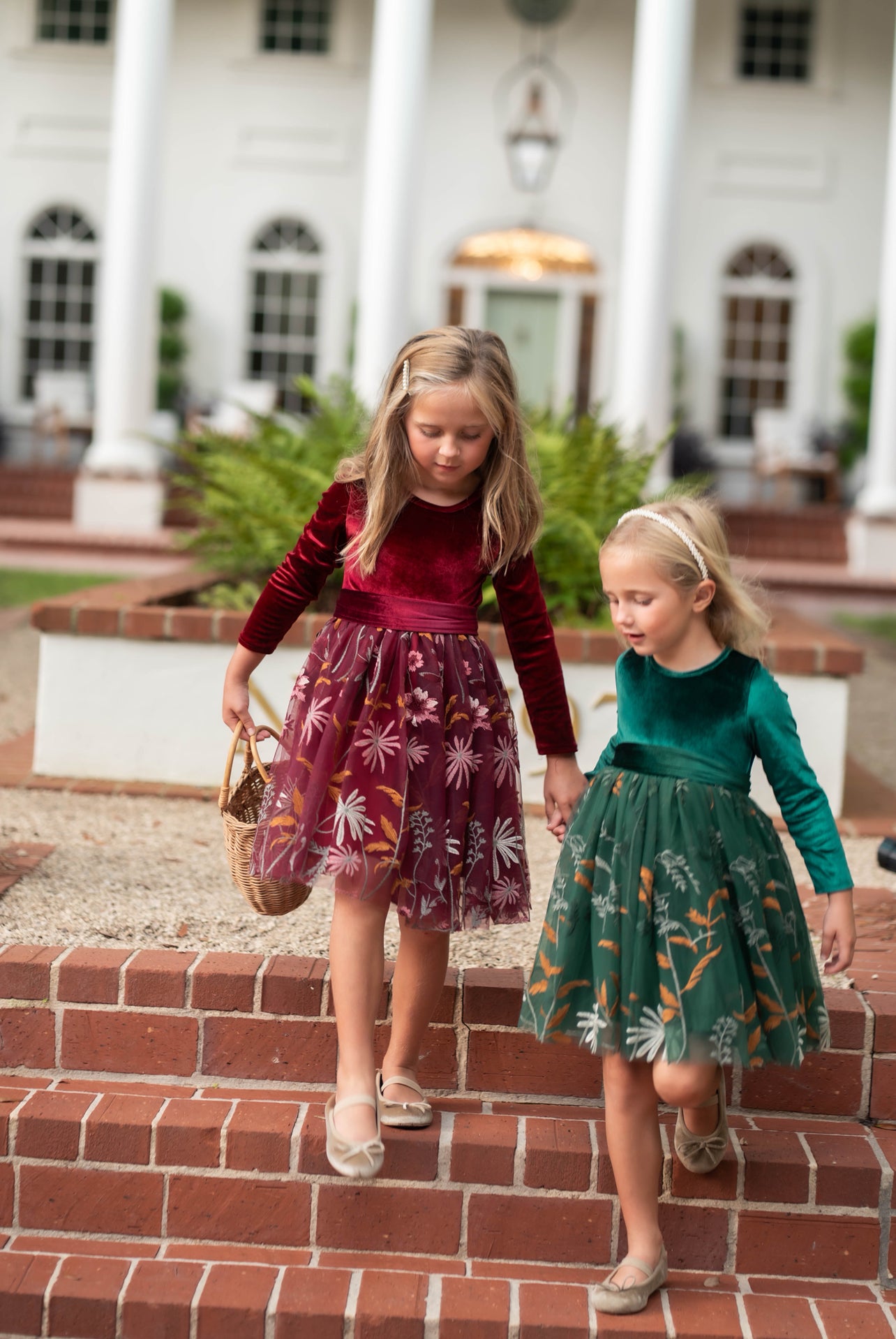Two girls wearing burgundy and hunter green velvet floral dresses together joyful
