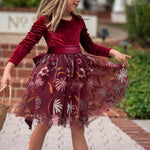 Girl twirling in burgundy velvet special occasion dress under holiday lights