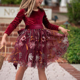 Girl twirling in burgundy velvet special occasion dress under holiday lights