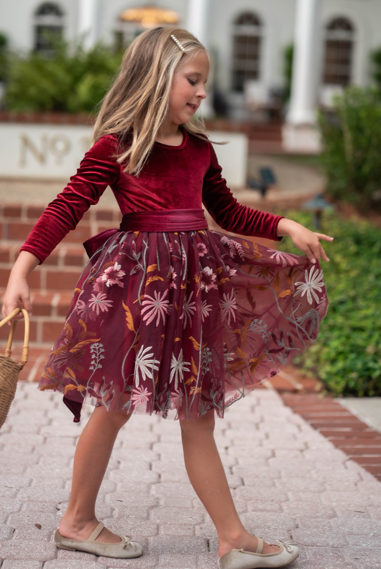 Girl twirling in burgundy velvet special occasion dress under holiday lights